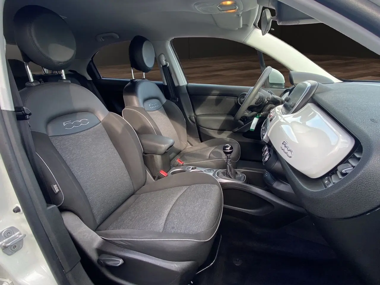 Vue intérieure côté conducteur d'une Fiat 500X blanche, sièges noirs avec logo 500 brodé sur appuie-tête.