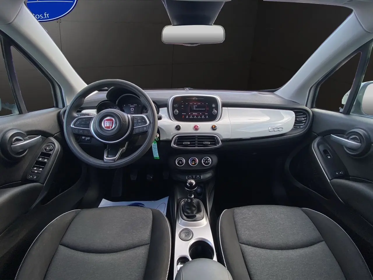 Vue intérieure frontale du tableau de bord blanc et noir de la Fiat 500X 2018 avec volant multifonction et boîte manuelle.