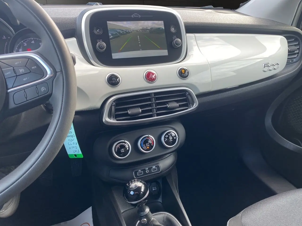 Vue intérieure du tableau de bord blanc brillant et console centrale noire d'une Fiat 500X avec écran tactile et levier de vitesse manuel.