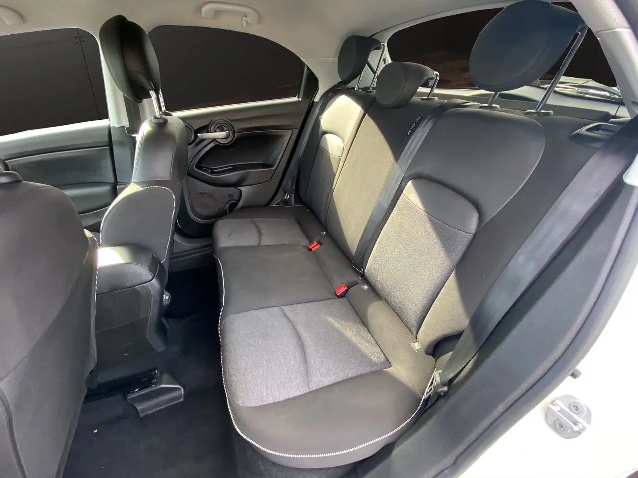 Vue intérieure arrière côté droit d'une Fiat 500X blanche, sièges noirs en tissu et cuir avec appuie-têtes réglables.