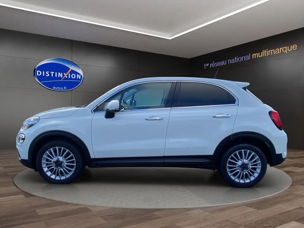 Profil côté gauche d'un FIAT 500X blanc 5 portes, avec jantes alliage et vitres teintées, en showroom.