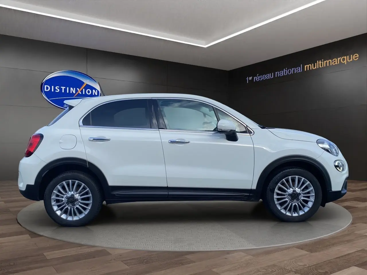 Profil côté gauche d'un FIAT 500X blanc 2018 avec jantes alliage et détails noirs urbains en intérieur showroom.
