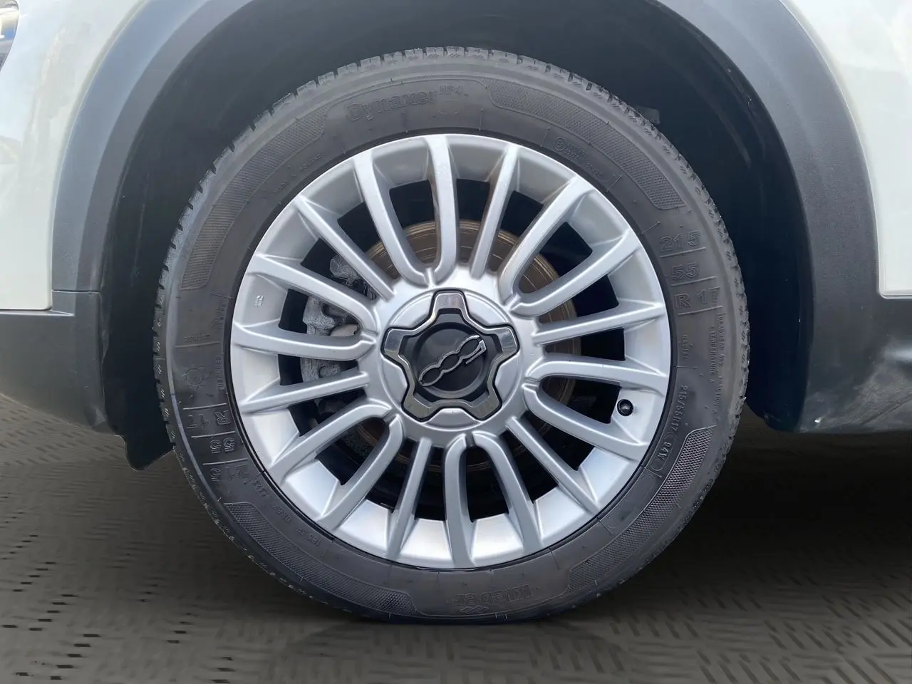 Gros plan sur la roue avant droite blanche d'une Fiat 500X 2018 avec jante alliage argentée au design étoilé.