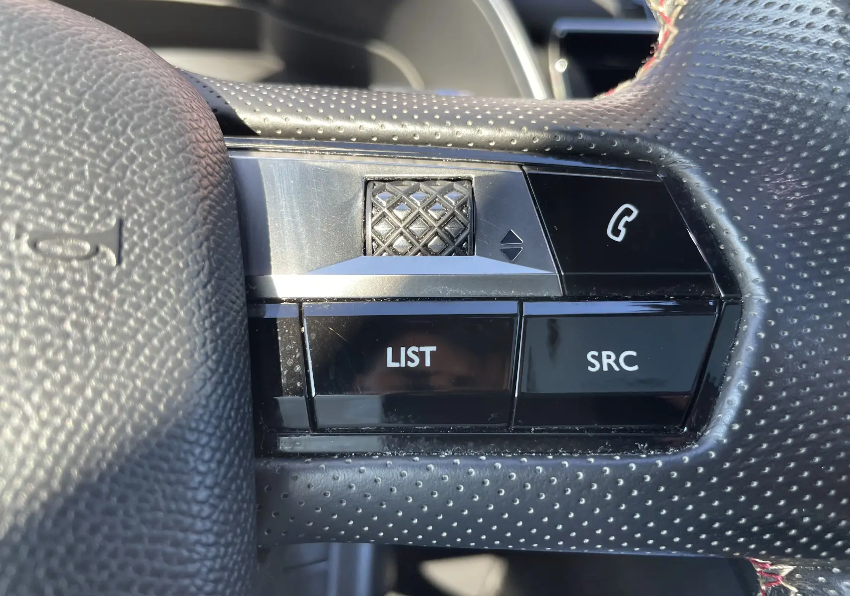 Gros plan sur les commandes gauche du volant perforé du DS7 2018 gris Artens, avec boutons LIST, SRC et téléphone.