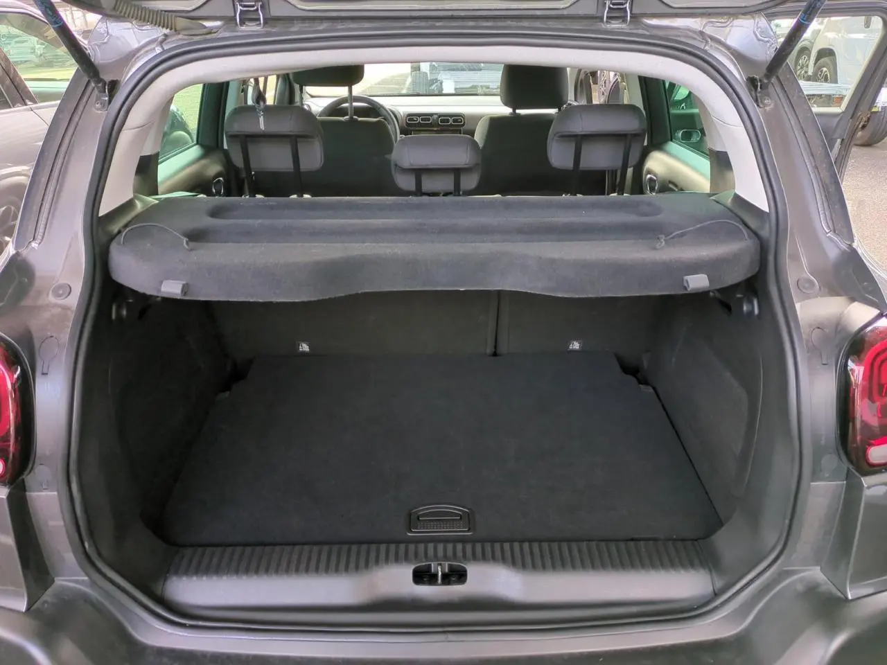 Vue arrière du coffre ouvert d'un Citroën C3 Aircross gris foncé avec cache-bagages et sièges arrière visibles.