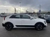 Vue de profil côté gauche d'un KIA Niro EV blanc 2024, version Active, avec jantes noires et toit noir contrastant.