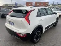 Vue 3/4 arrière d'un KIA Niro EV blanc 2024, version Active, avec feux arrière en forme de boomerang et jantes noires.