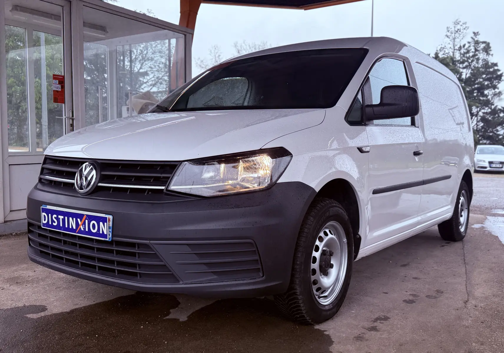 Volkswagen Caddy Maxi Long blanc vue 3/4 avant droit sous abri avec calandre noire et jantes acier.