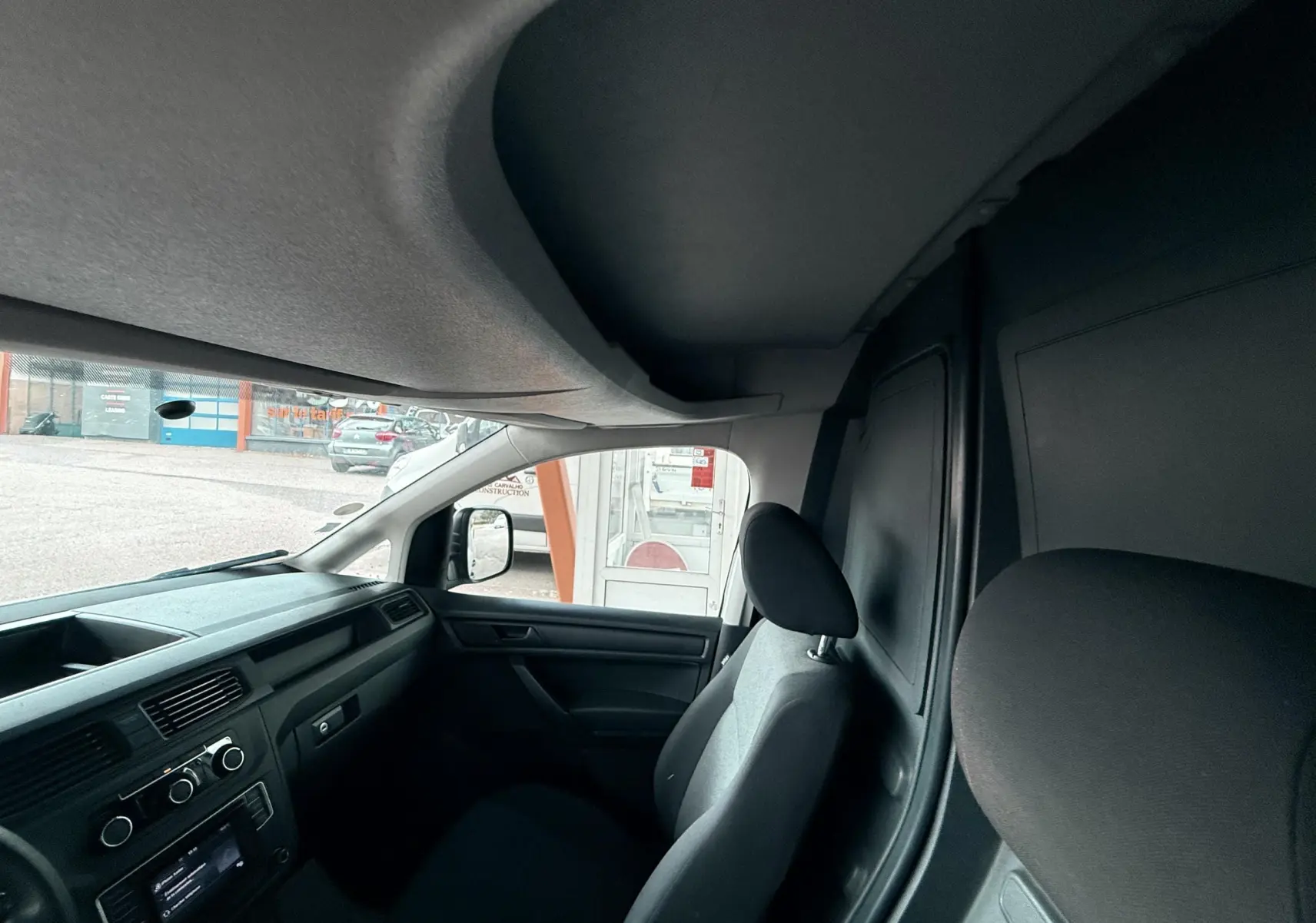 Vue intérieure côté passager du Volkswagen Caddy Maxi Long blanc, montrant les sièges et le tableau de bord noir.