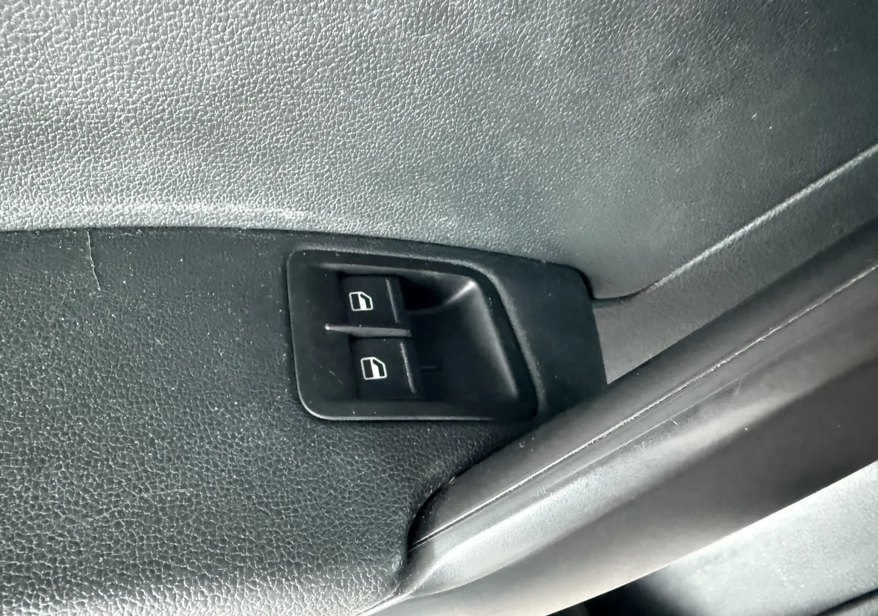 Gros plan sur les commandes de lève-vitres noires intégrées à la portière intérieure côté conducteur du Volkswagen Caddy blanc.