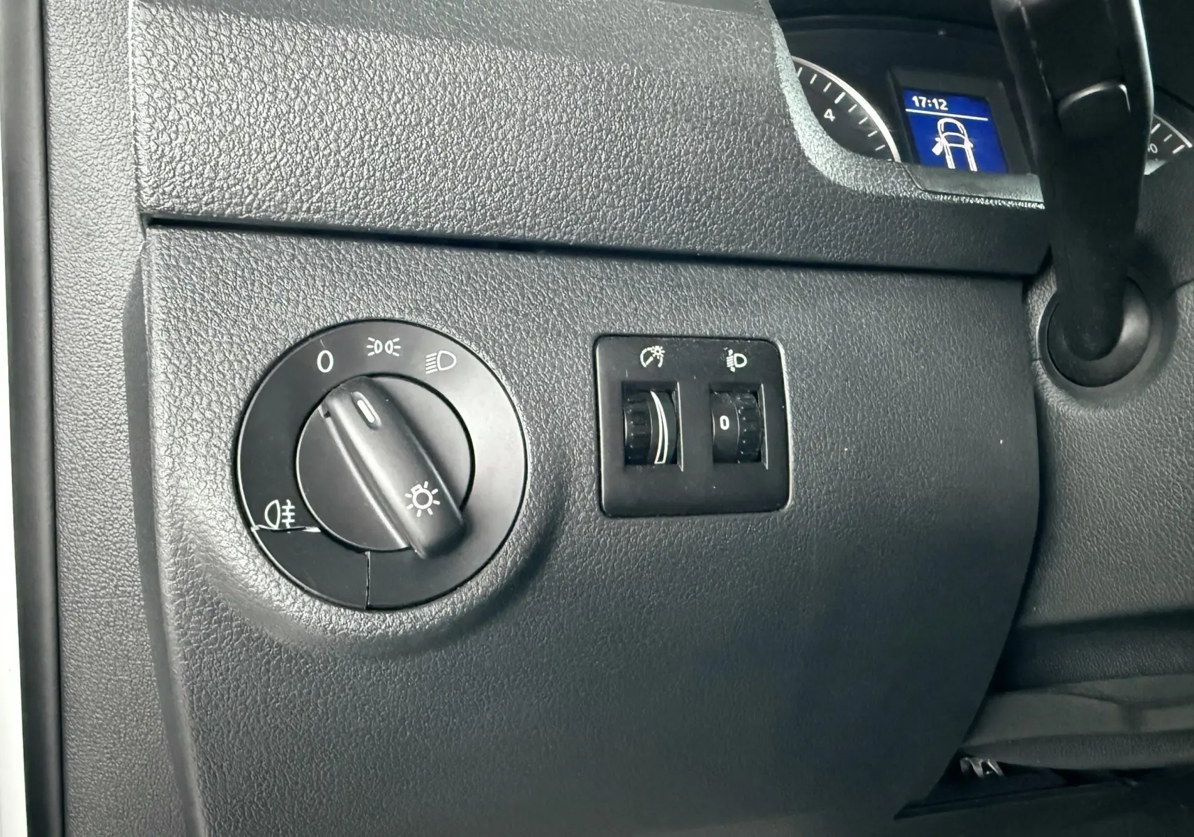 Gros plan sur le tableau de bord noir du Volkswagen Caddy, montrant les commandes d’éclairage et un écran digital partiel.