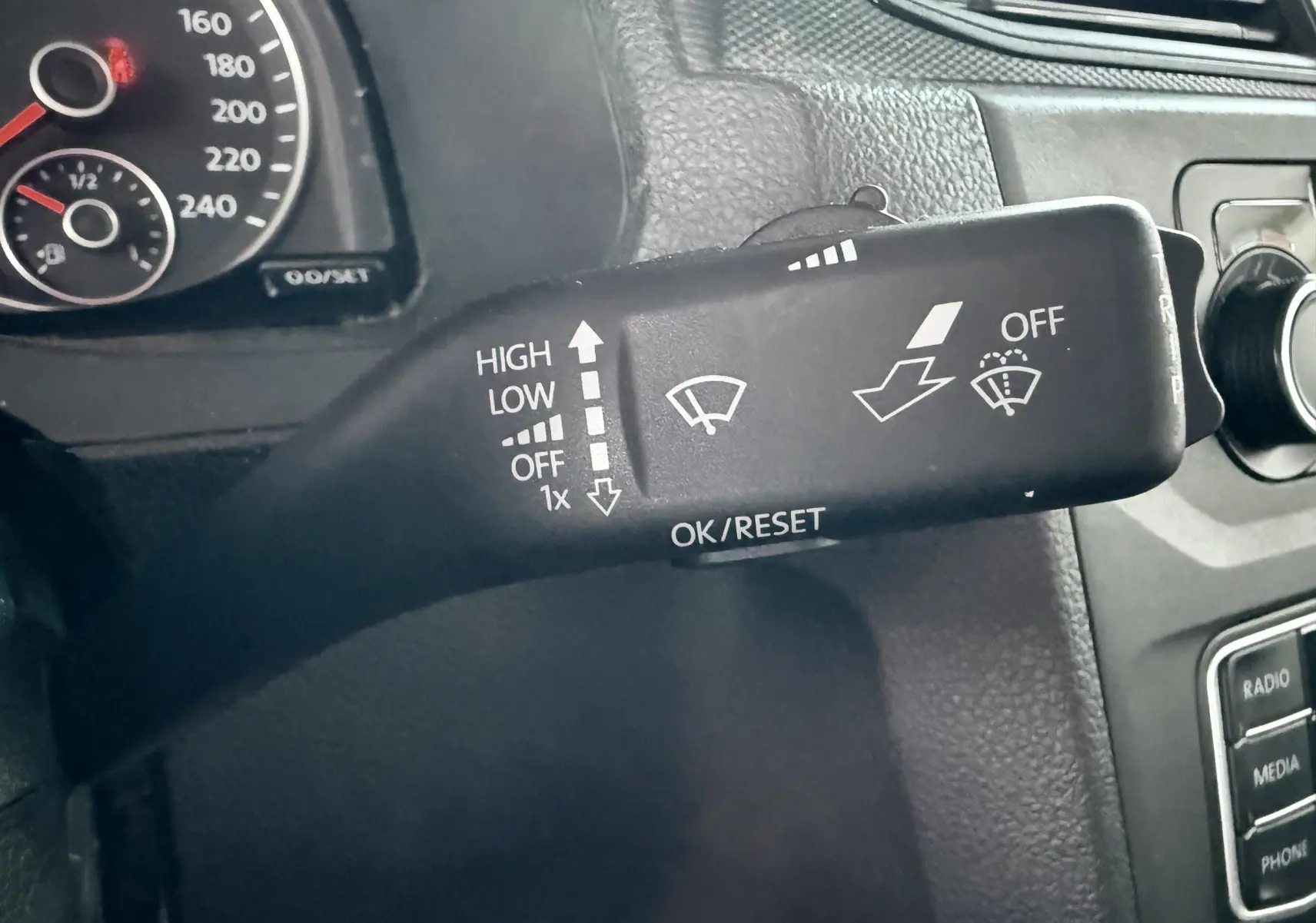 Gros plan sur la commande d’essuie-glace à gauche du volant dans l’habitacle noir du Volkswagen Caddy blanc.