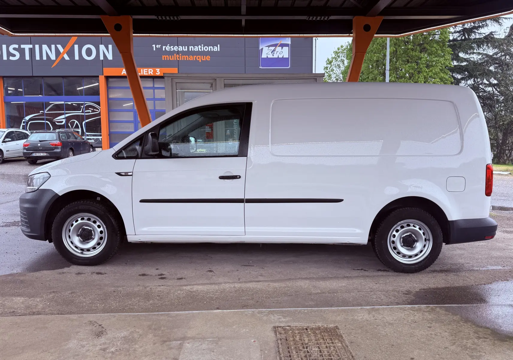 Vue de profil côté gauche d’un Volkswagen Caddy Maxi Long blanc, utilitaire avec jantes acier sous abri.