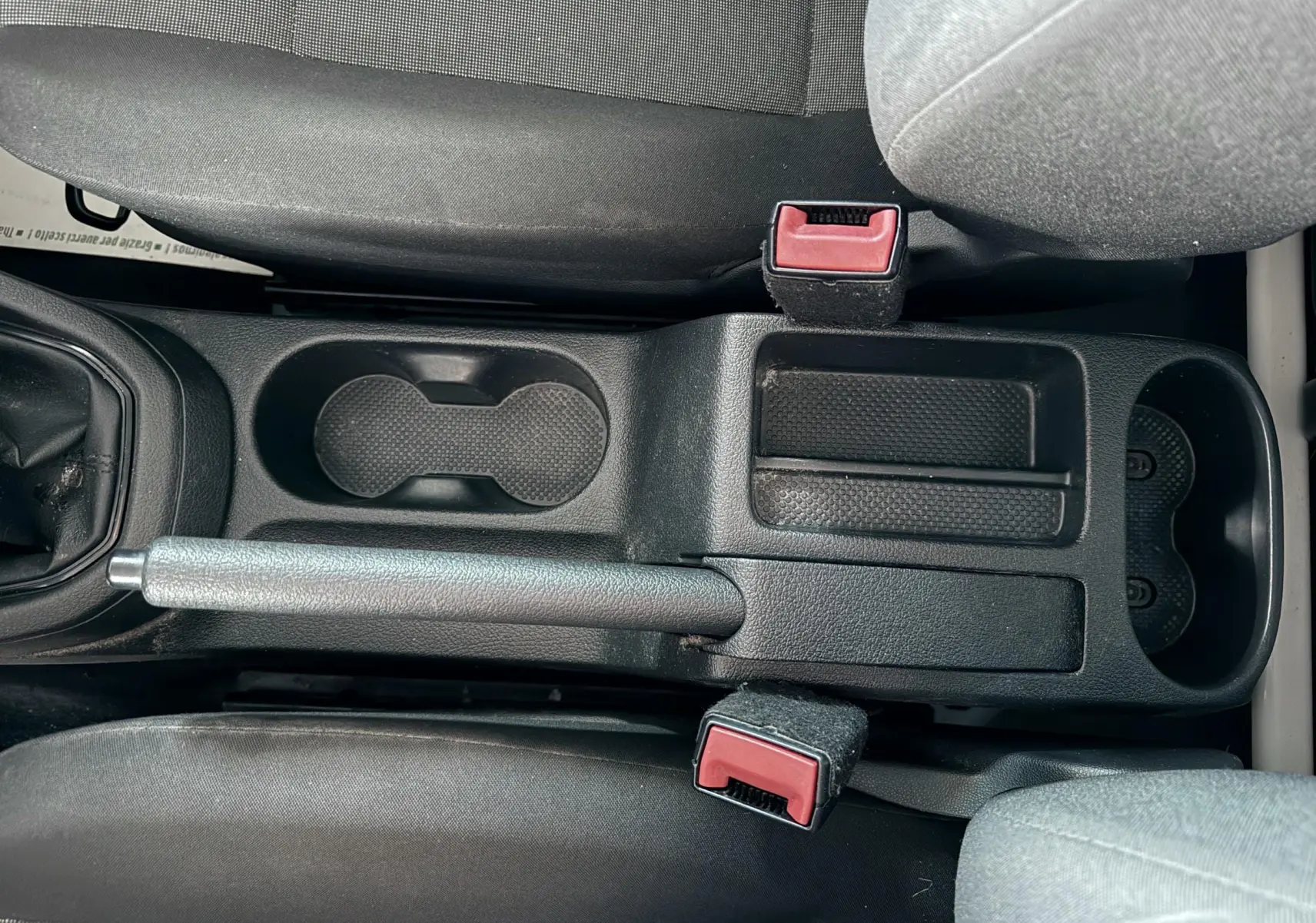 Vue plongeante sur la console centrale noire du Volkswagen Caddy avec frein à main et porte-gobelets entre les sièges gris.