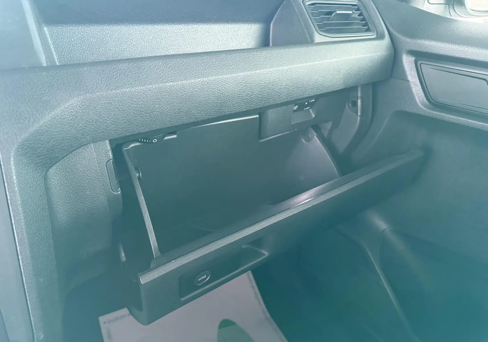 Vue intérieure côté passager du Volkswagen Caddy blanc 2017, boîte à gants ouverte avec tableau de bord noir.