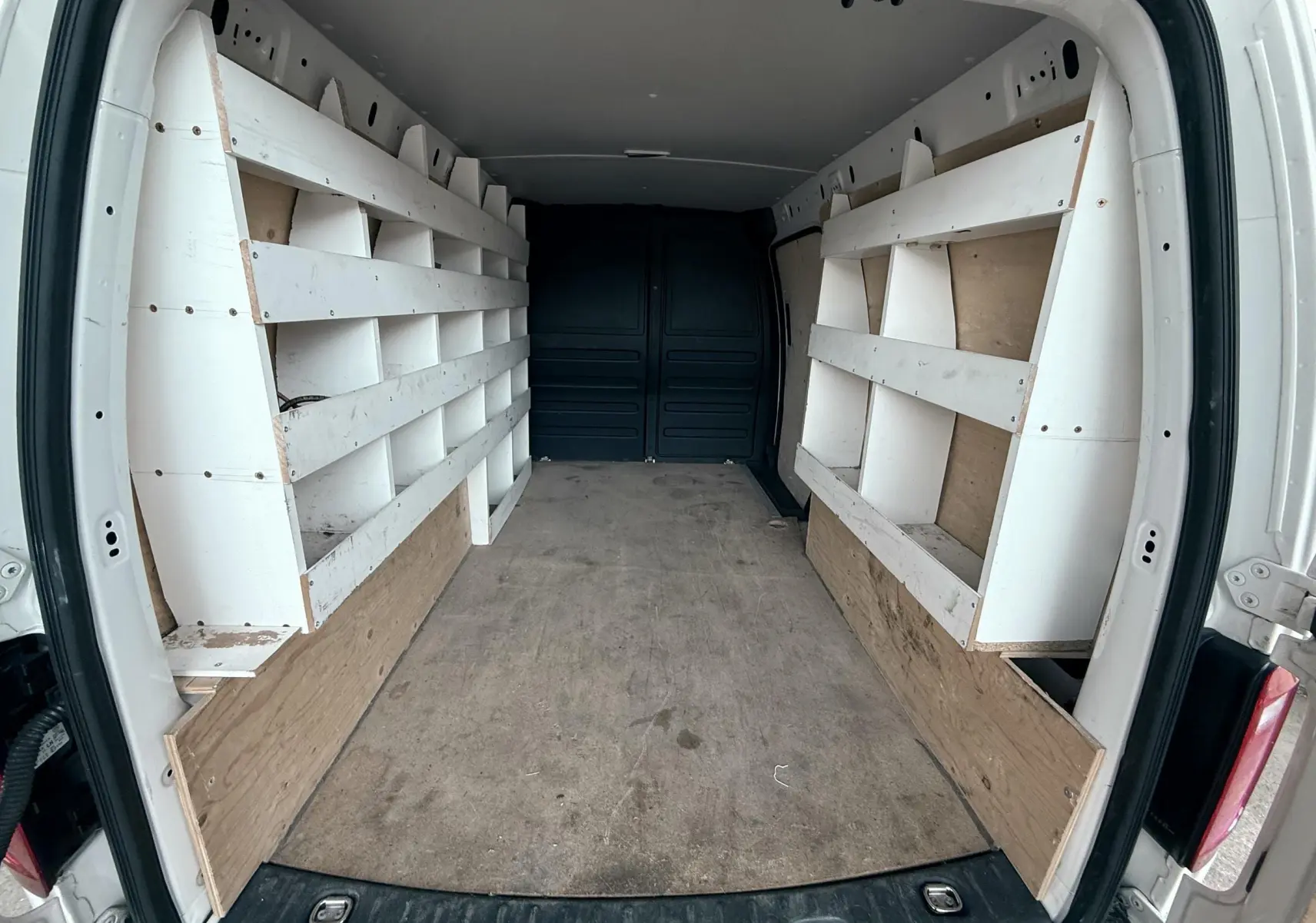 Vue intérieure arrière du Volkswagen Caddy Maxi Long blanc de 2017 avec étagères de rangement en bois intégrées.