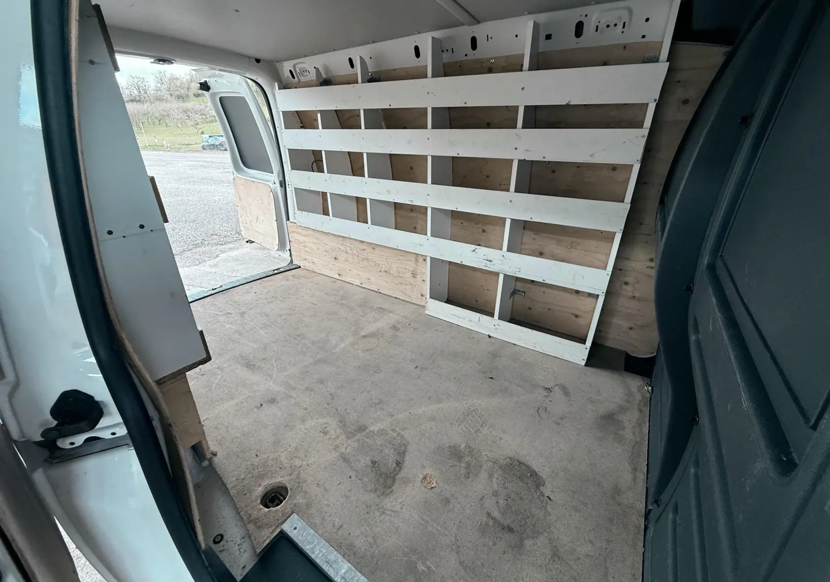 Vue intérieure arrière du Volkswagen Caddy Maxi Long blanc, montrant l'espace de chargement avec étagères en bois sur le côté droit.