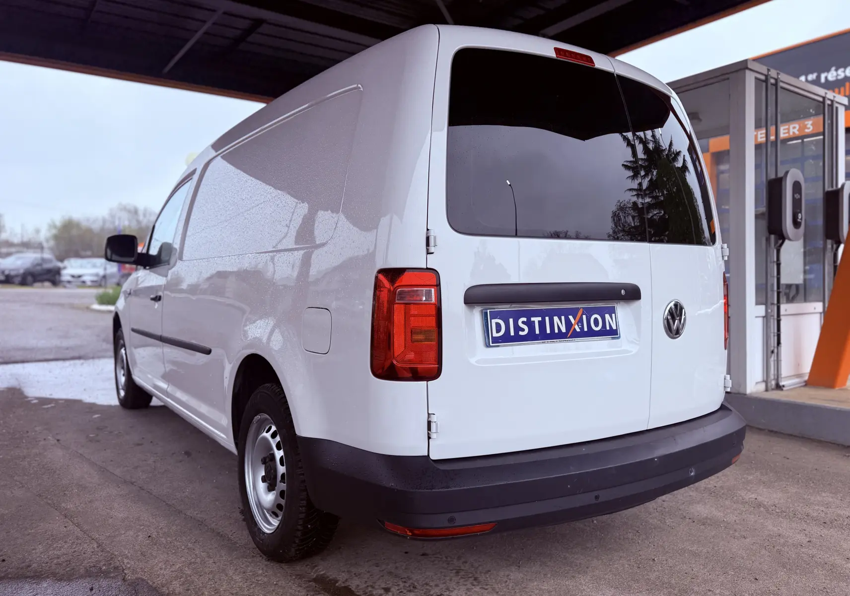 Vue 3/4 arrière droite d’un utilitaire Volkswagen Caddy Maxi Long blanc stationné sous abri, avec vitres arrière teintées.
