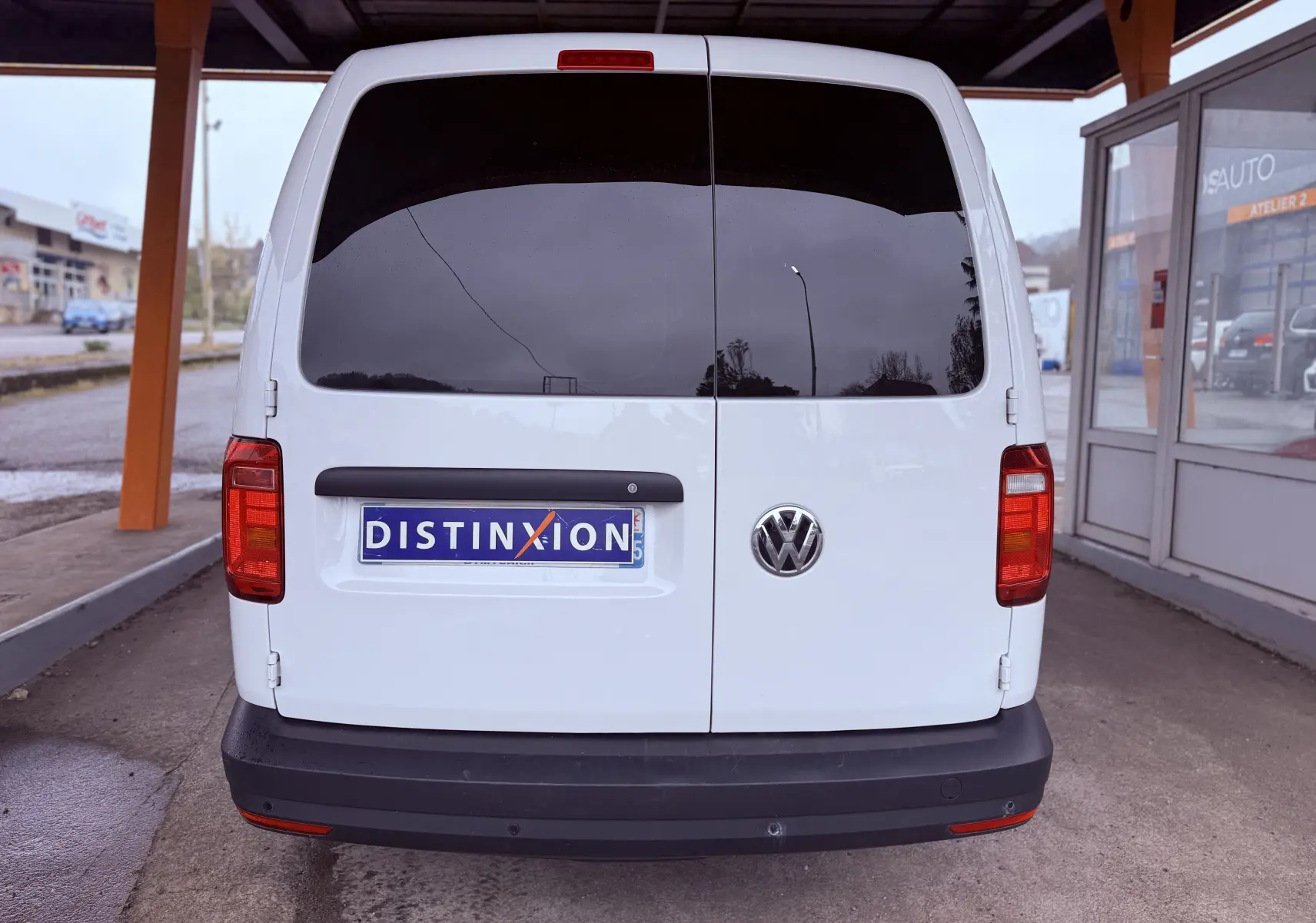 Vue arrière d'un Volkswagen Caddy Maxi Long blanc garé sous abri, avec vitres arrière teintées et plaque Distinxion.