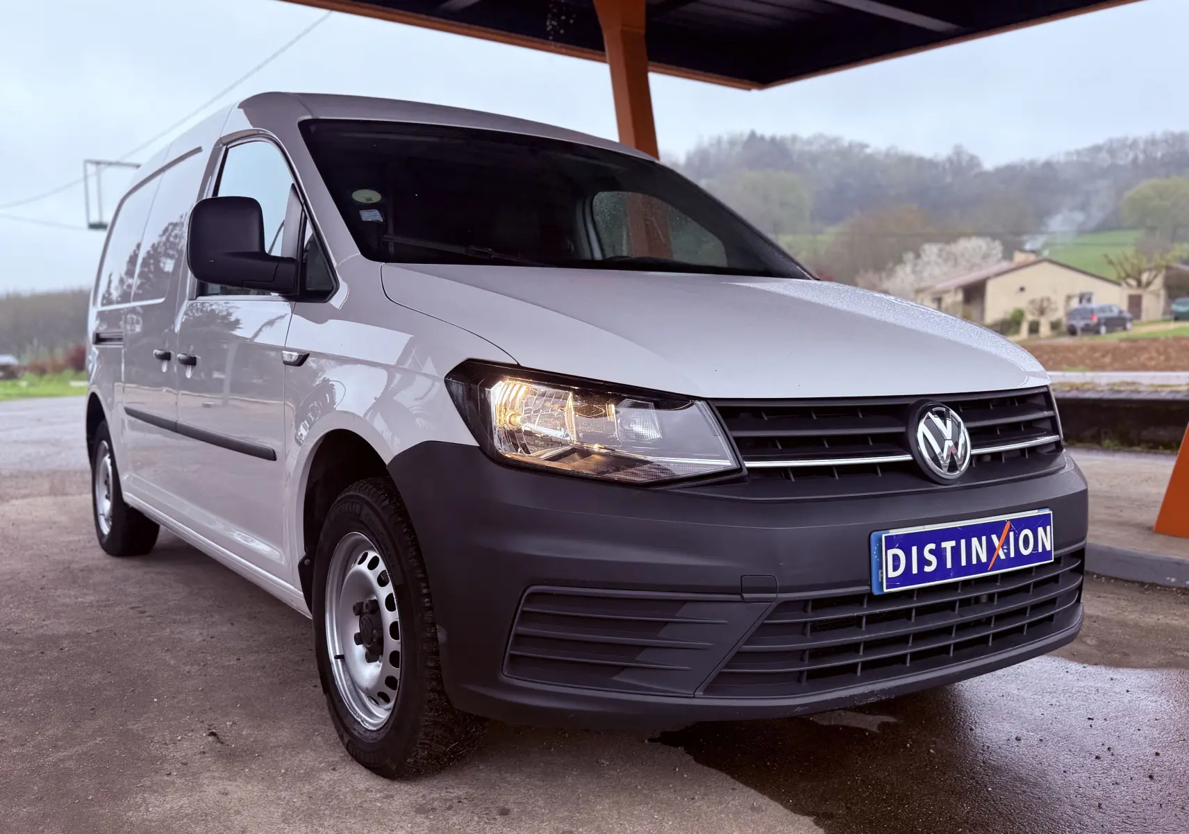 Vue 3/4 avant droit d'un Volkswagen Caddy Maxi Long blanc avec pare-chocs noir mat sous un abri.