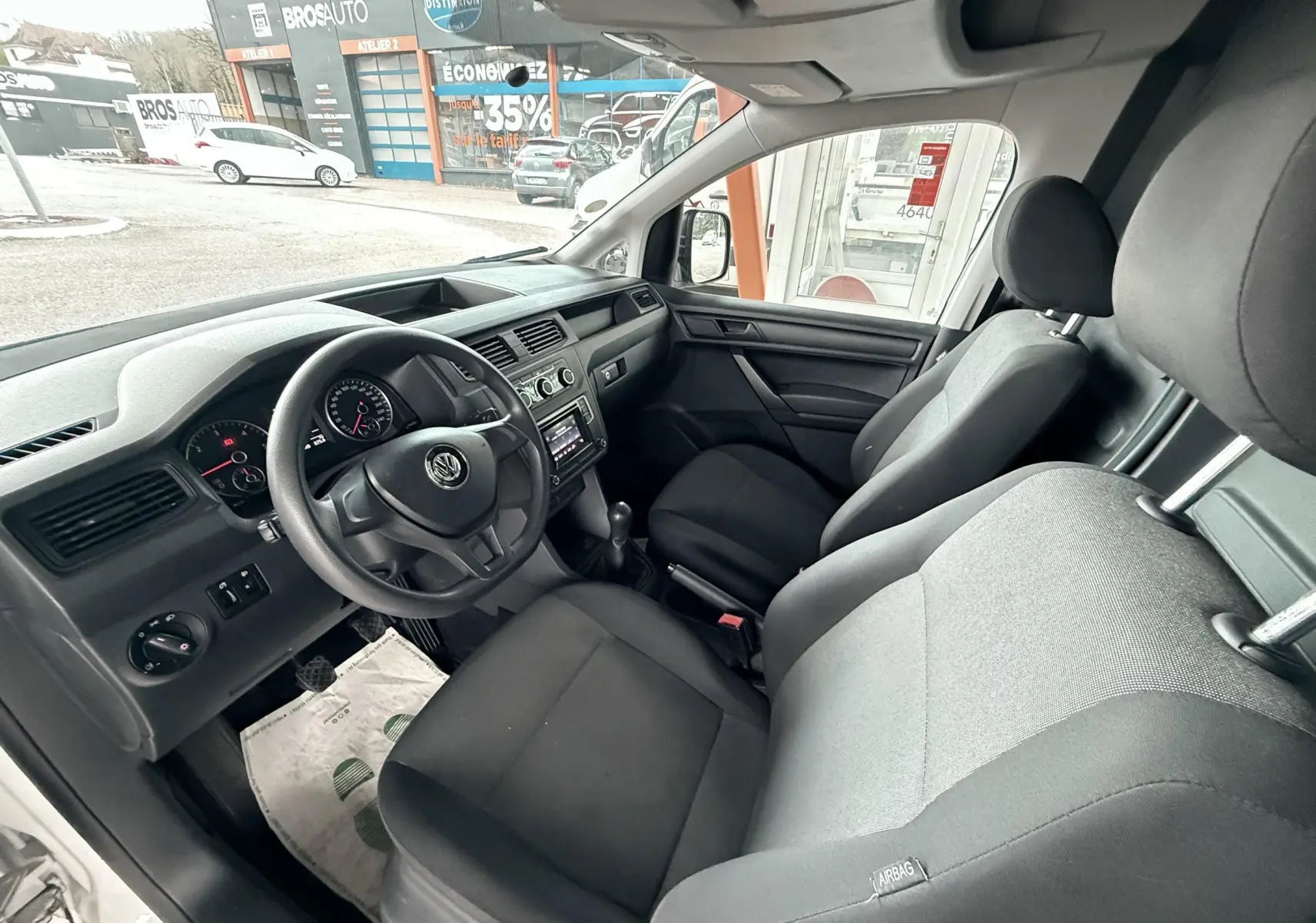 Vue intérieure côté conducteur du Volkswagen Caddy Maxi Long 2017, sièges tissu noir et tableau de bord gris foncé.