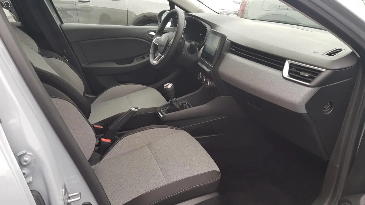 Vue intérieure côté conducteur de la Renault Clio gris 2025, montrant sièges tissu bicolore et tableau de bord moderne.