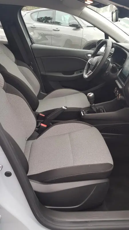 Vue intérieure côté conducteur de la Renault Clio gris 2025 avec sièges tissu bicolore et boîte manuelle visible.