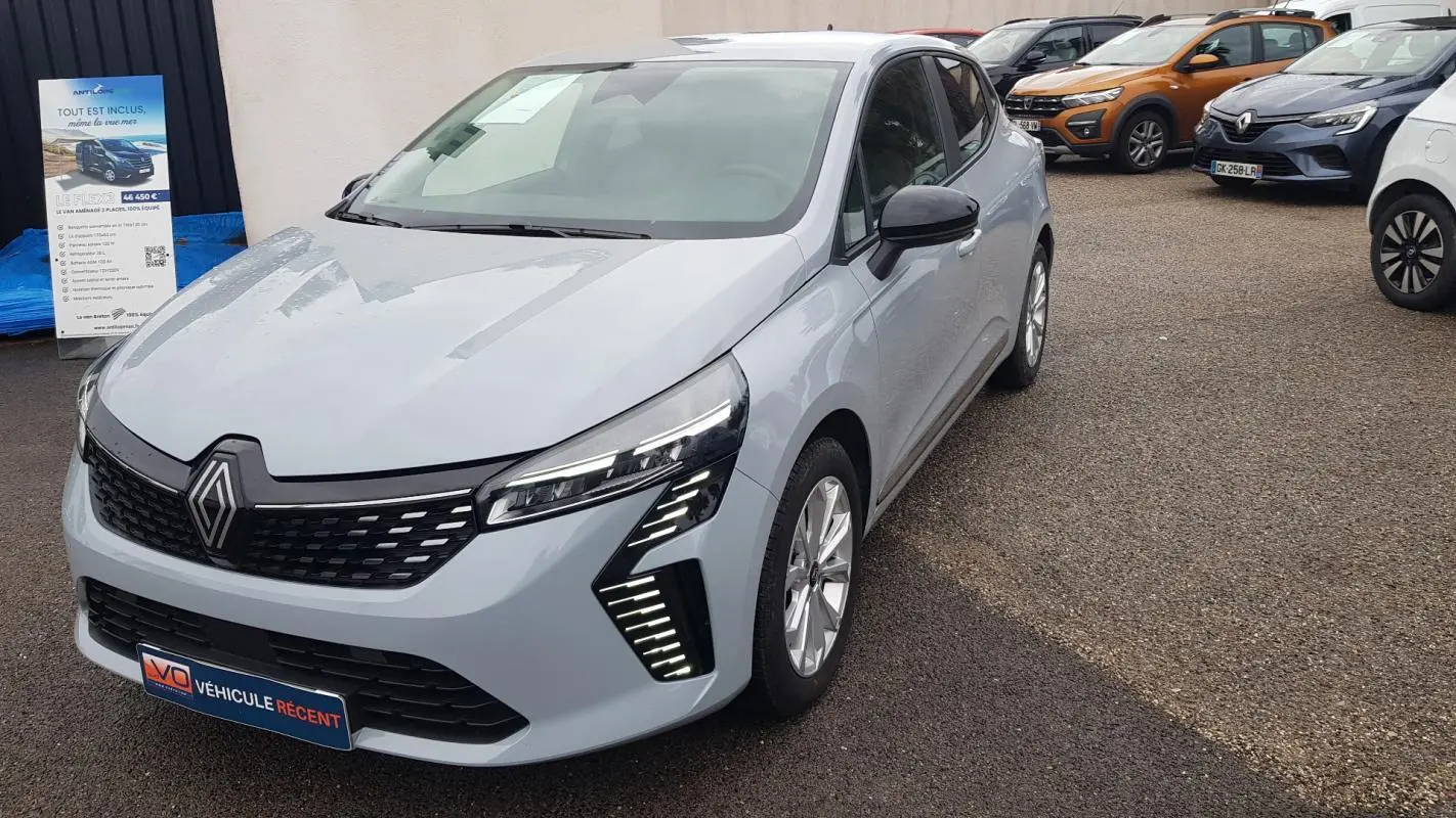 Renault Clio gris vue 3/4 avant droit, avec signature lumineuse LED distinctive et calandre noire.