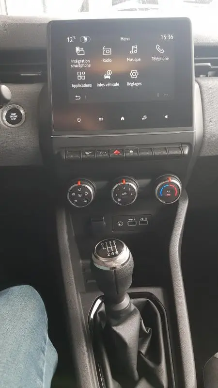 Vue centrale de l'intérieur de la Renault Clio 2025 gris, avec écran tactile, commandes climatisation et levier de vitesse manuel.