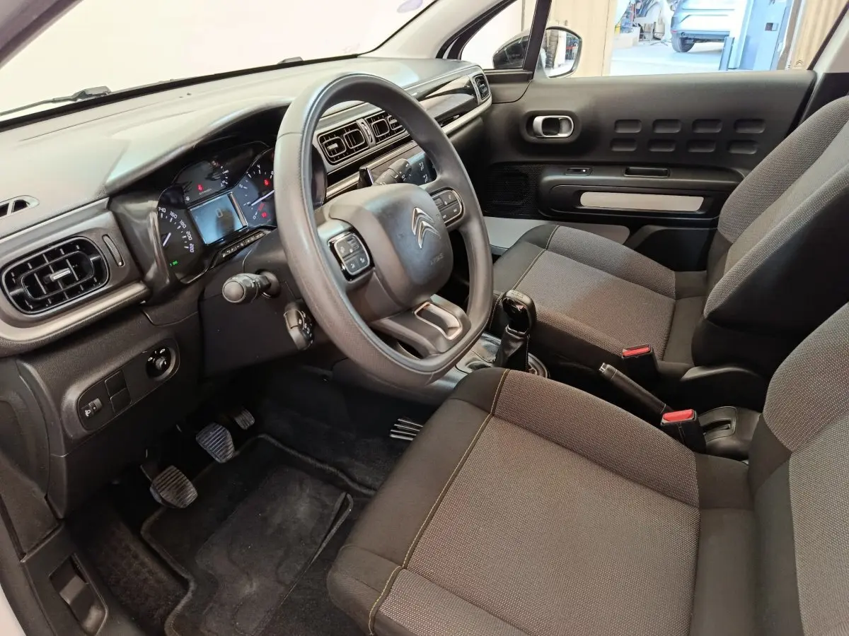 Vue intérieure côté conducteur de la Citroën C3 2022, volant multifonctions, sièges tissu gris et tableau de bord noir.
