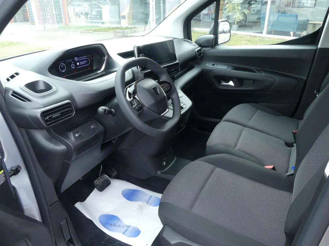 Vue intérieure côté conducteur du Peugeot Partner XL 2025, avec tableau de bord moderne et sièges tissu gris.