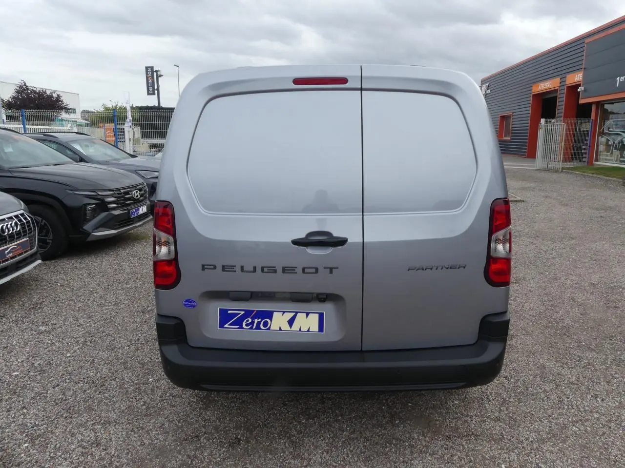 Vue arrière d'un Peugeot Partner gris métallisé 2025 avec portes battantes et plaque d'immatriculation ZeroKM visible.