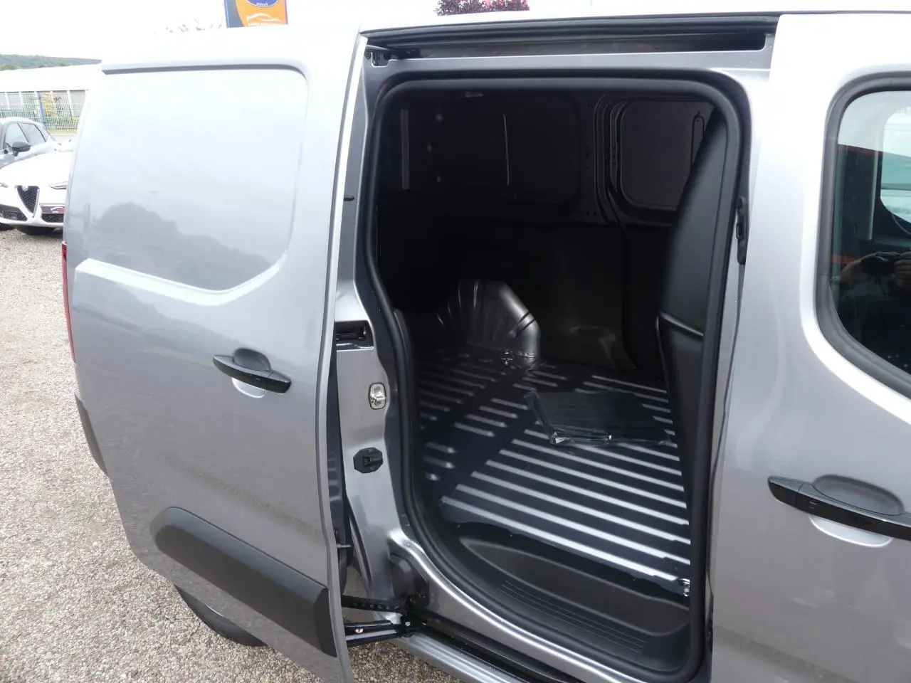 Vue côté droit du Peugeot Partner XL gris métallisé avec porte coulissante ouverte sur l'espace de chargement vide.