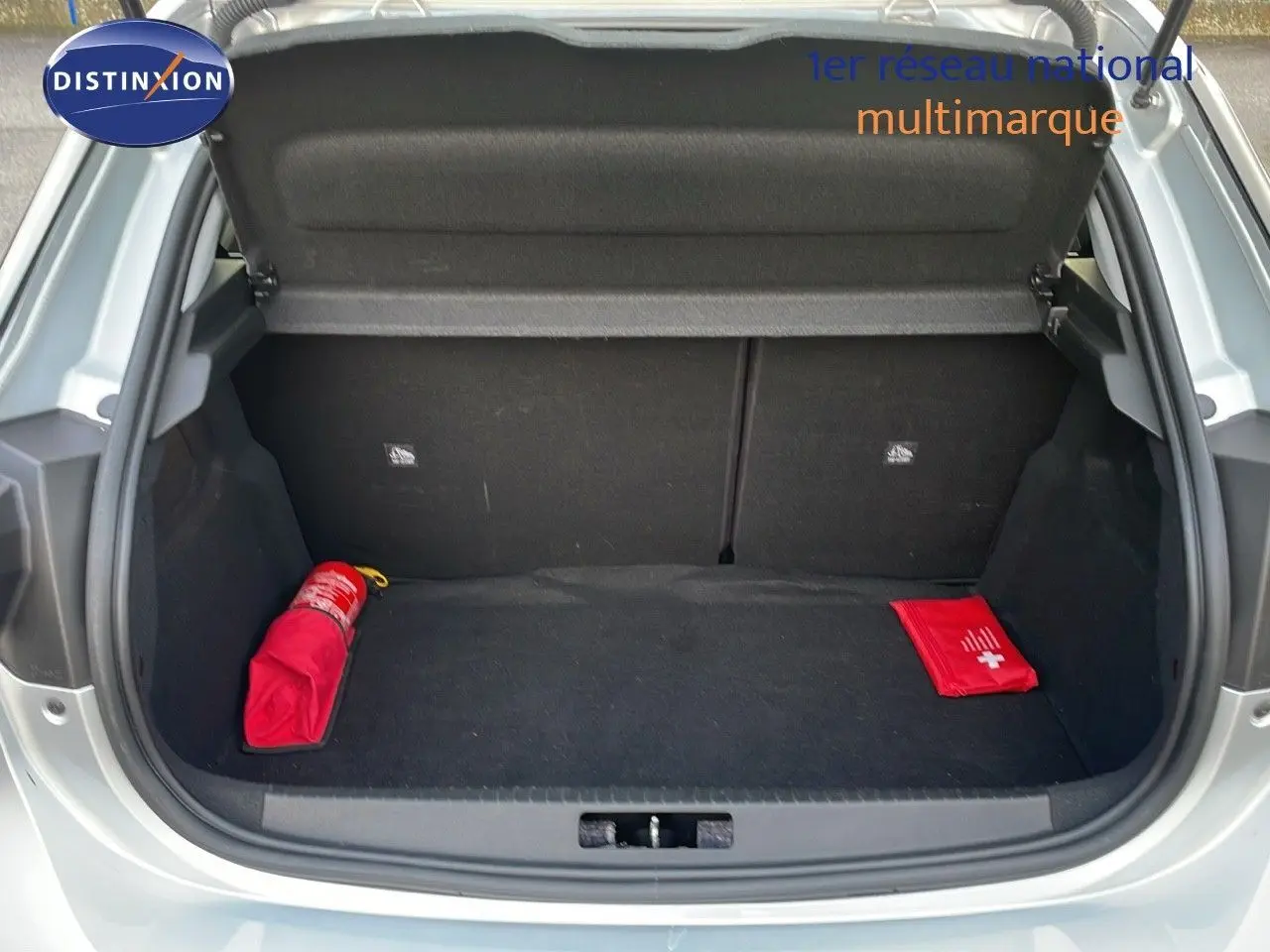 Coffre ouvert d'une Opel Corsa gris kristall metal 2022, montrant un extincteur et une trousse de secours rouges.