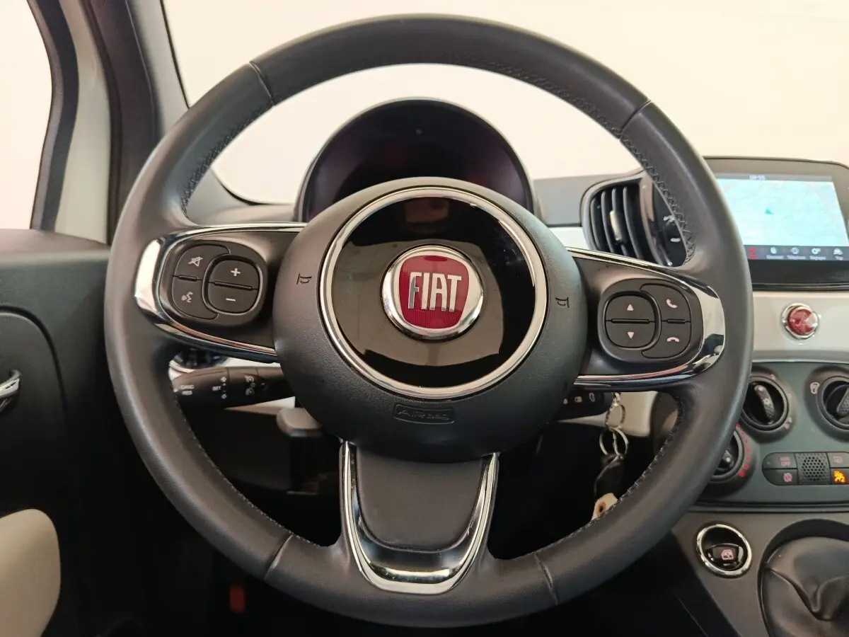 Vue rapprochée du volant cuir noir multifonctions d'une Fiat 500 blanche avec tableau de bord et écran tactile visible.
