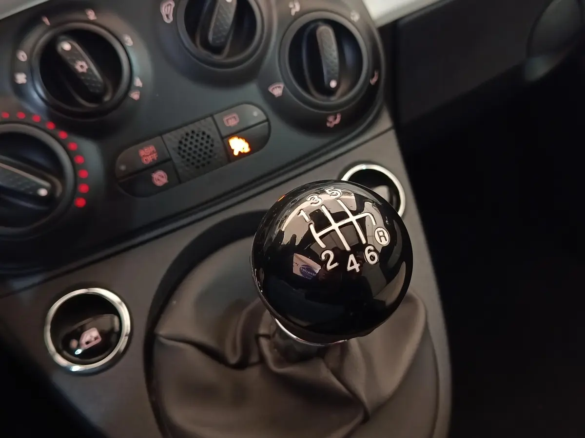 Gros plan sur le levier de vitesses manuel noir de la FIAT 500 Hybrid, avec commandes de climatisation en arrière-plan.