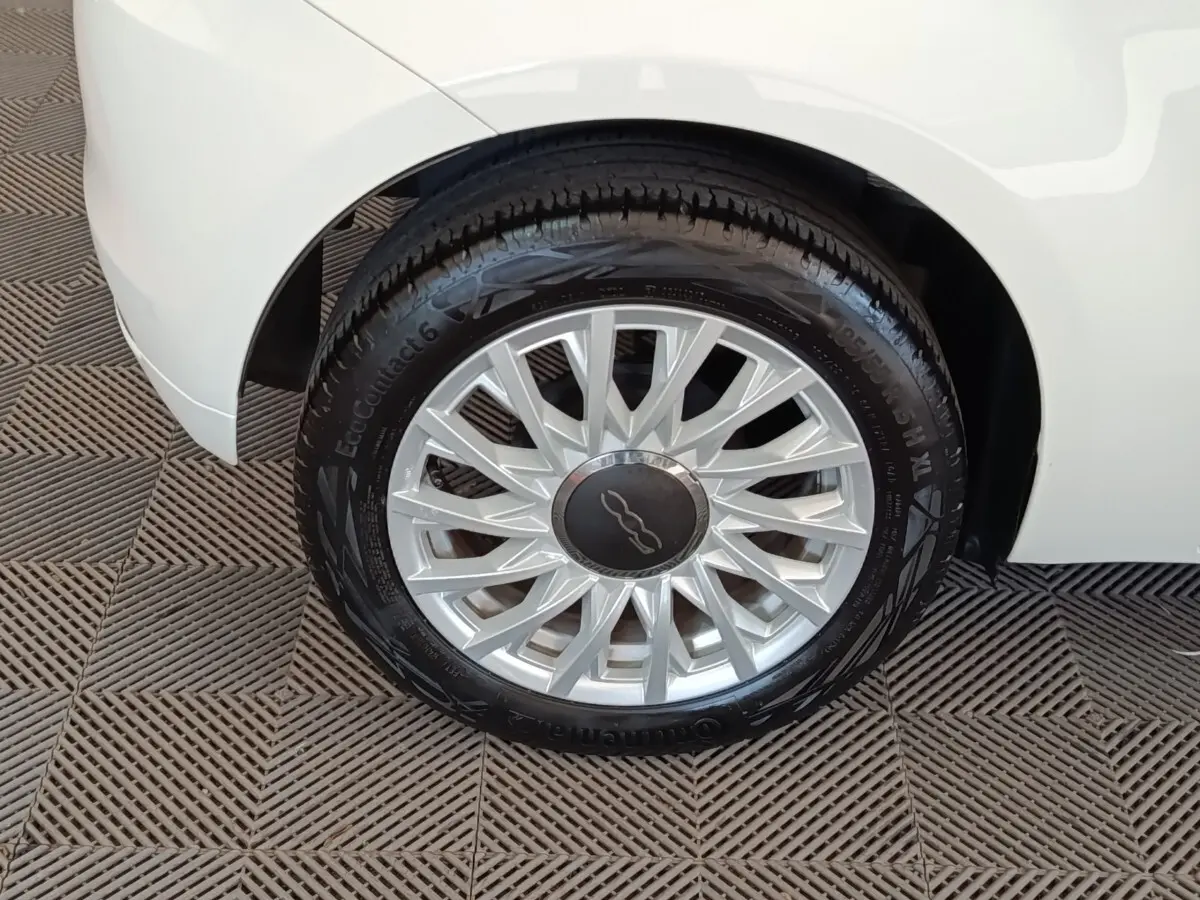 Gros plan sur la roue avant droite d’une FIAT 500 blanche, mettant en valeur la jante argentée au design étoilé.
