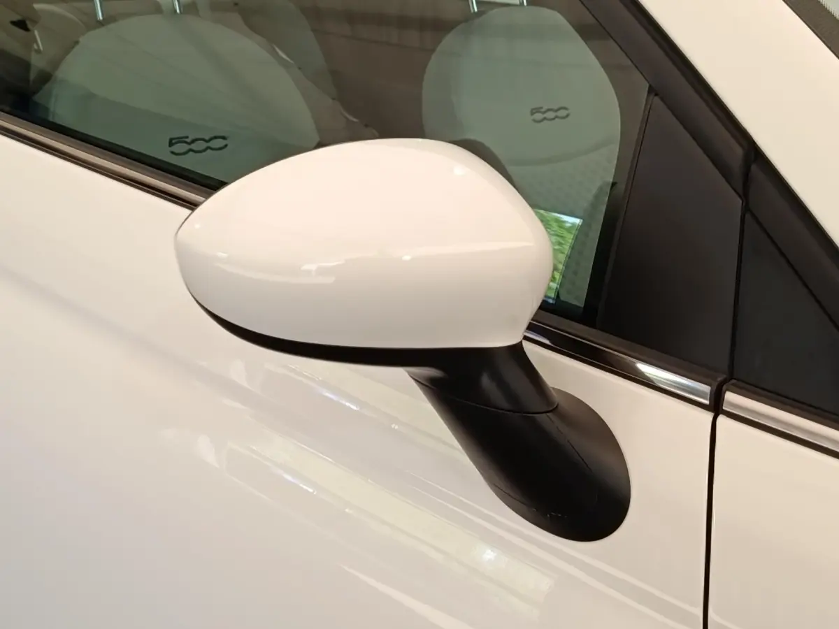 Rétroviseur côté gauche blanc de la Fiat 500 Hybrid 2022 avec sièges clairs et logo 500 visible à l'intérieur.