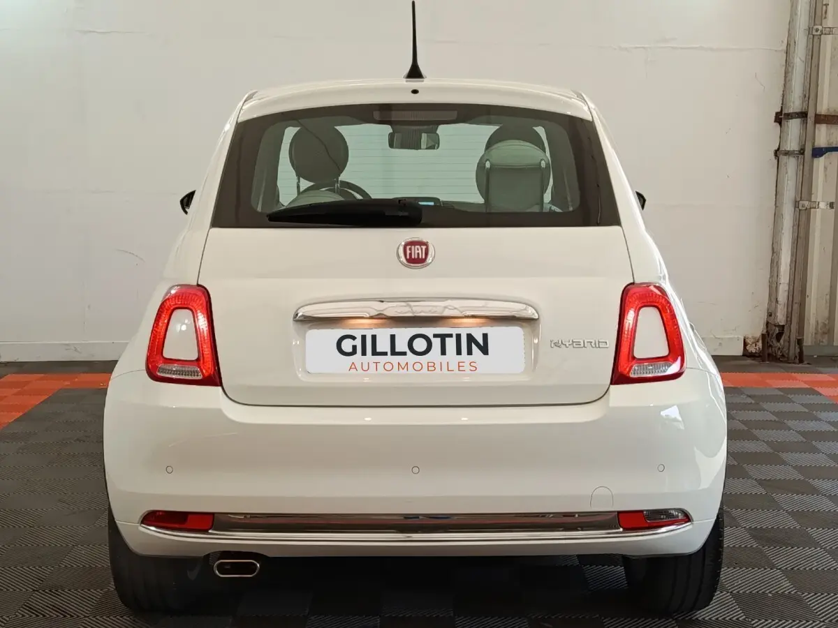 Vue arrière d'une FIAT 500 Hybrid blanche, avec feux arrière allumés et logo FIAT visible sur un sol à damier.