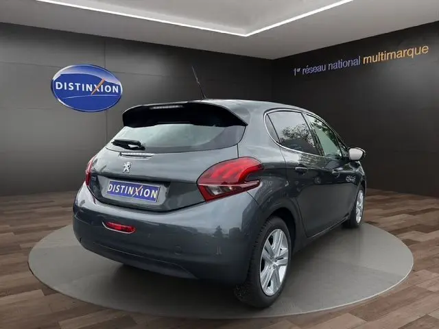 Vue 3/4 arrière droite d'une Peugeot 208 gris platinium 2017 dans un showroom avec logo Distinxion en arrière-plan.