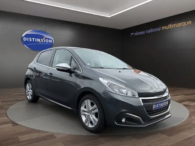 Peugeot 208 gris platinium vue 3/4 avant droit, avec rétroviseurs chromés et feux LED, en showroom.