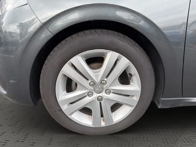 Gros plan sur la roue avant gauche d'une Peugeot 208 gris platinium, mettant en valeur la jante alliage à 5 branches doubles.