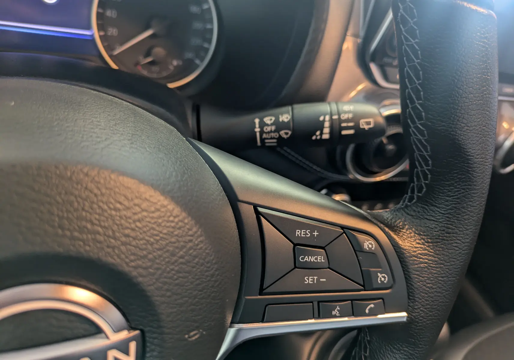 Gros plan sur le volant en cuir noir du Nissan Juke 2024, montrant les commandes de régulateur de vitesse à droite.