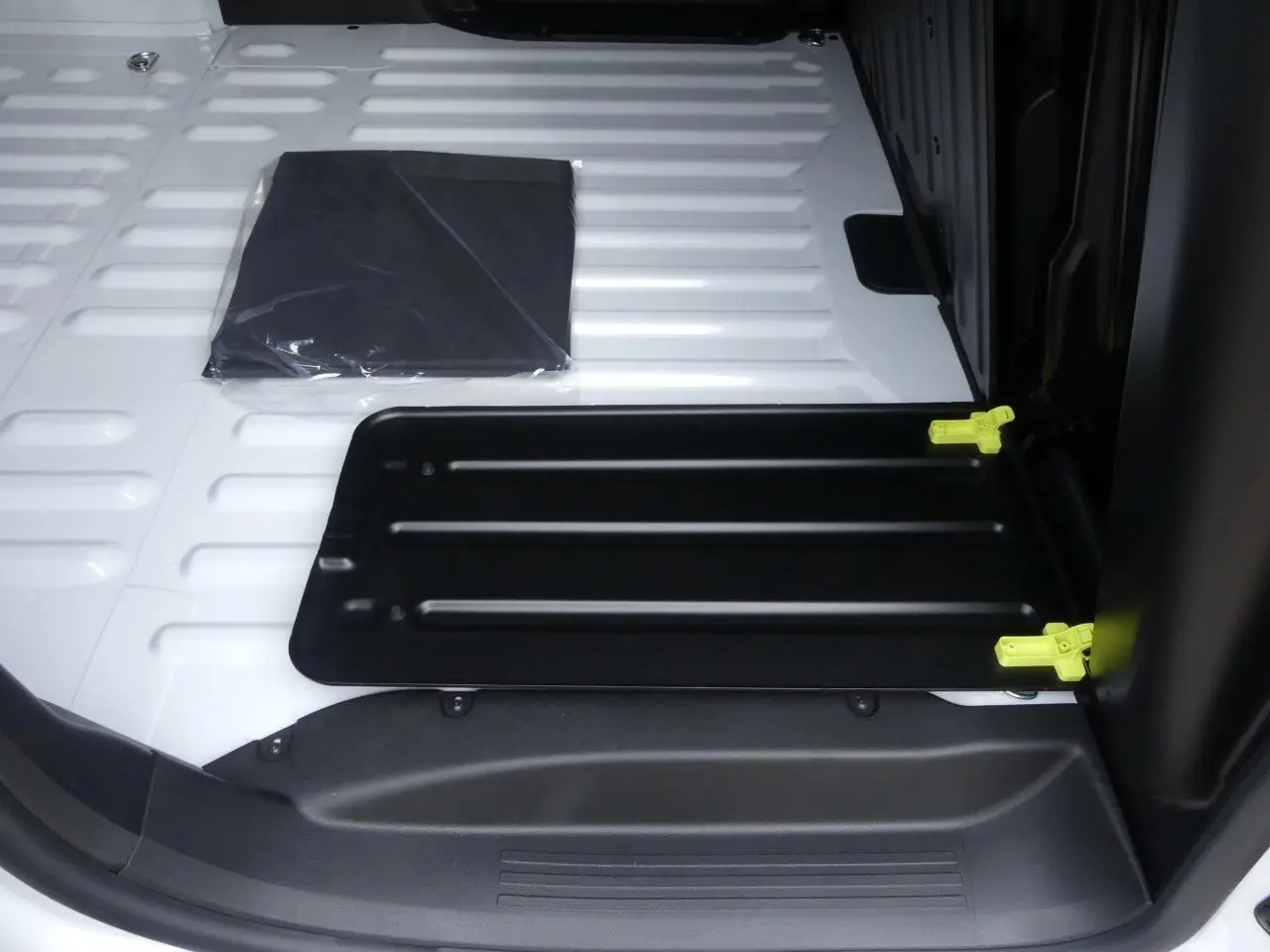 Vue rapprochée de la zone de chargement blanche du Peugeot Partner XL avec trappe noire et fixations jaunes visibles.