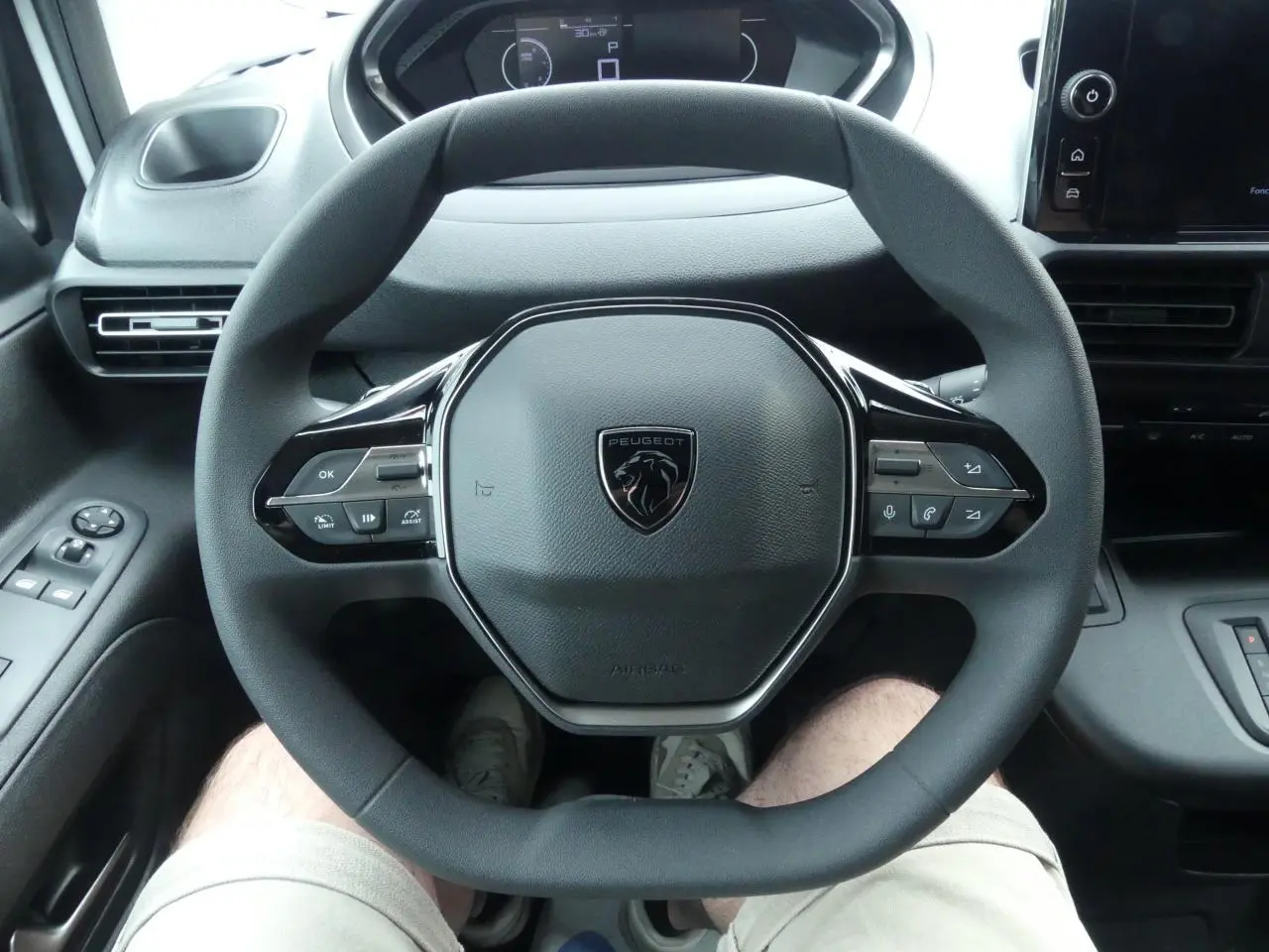 Vue rapprochée du volant multifonctions noir avec logo Peugeot au centre dans l'habitacle du Partner XL blanc 2025.