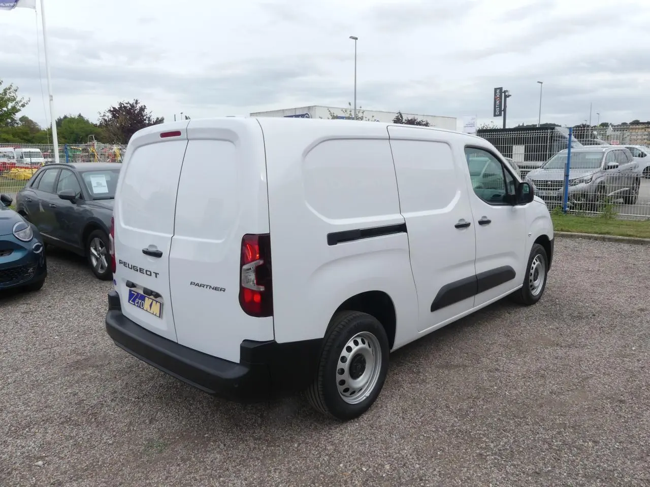 Vue 3/4 arrière droite du Peugeot Partner blanc avec portes arrière battantes et protections latérales noires.
