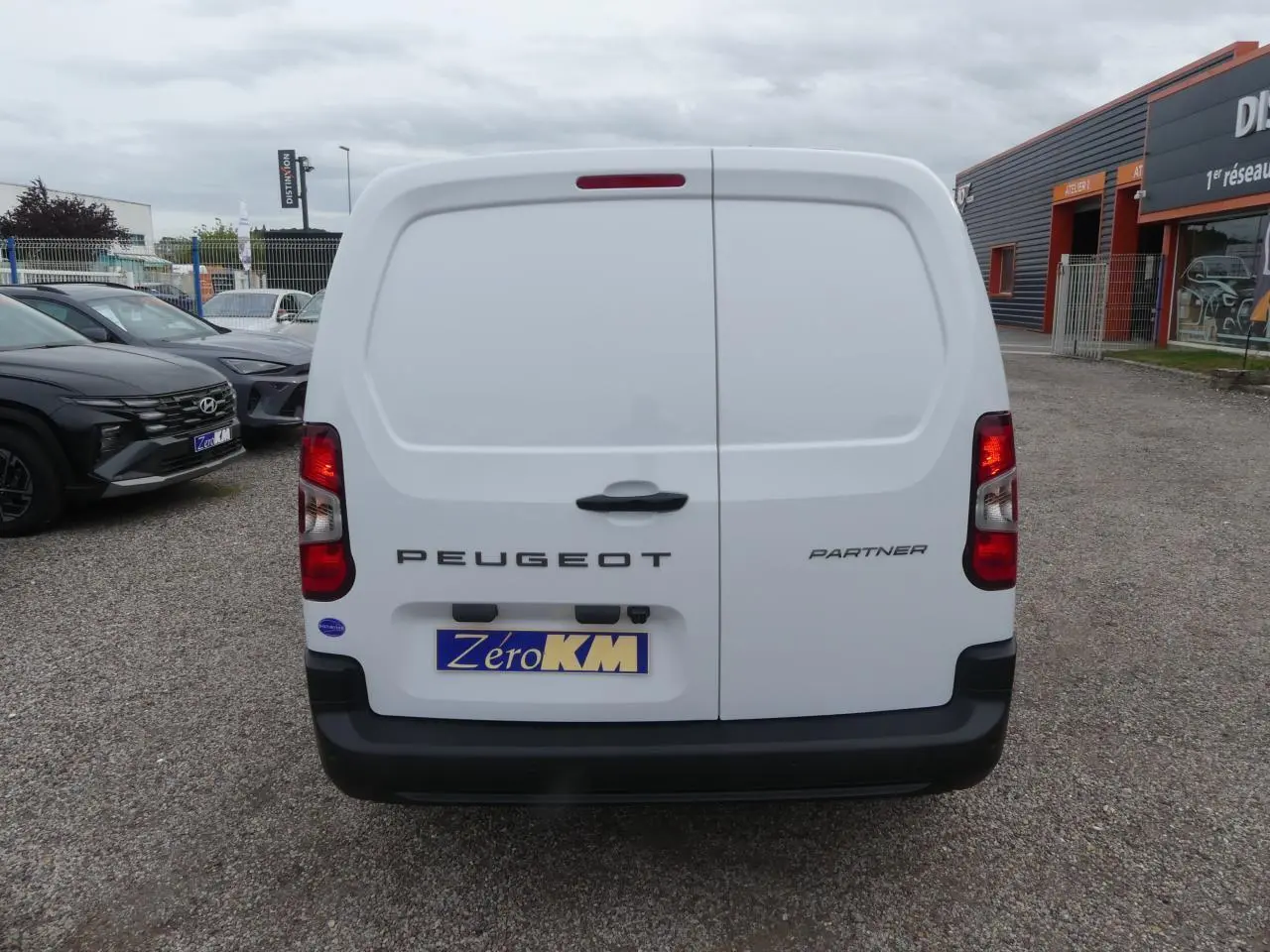 Vue arrière d'un Peugeot Partner blanc avec portes battantes et pare-chocs noir sur un parking.