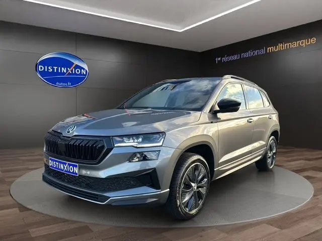 SUV Skoda Karoq gris graphite en 3/4 avant droit, avec jantes alliage noires et calandre marquée.