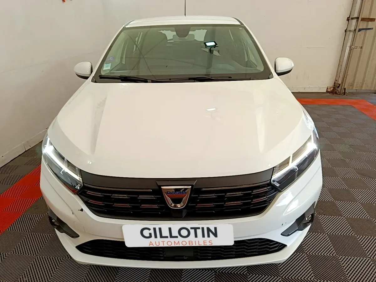 Vue avant d'une Dacia Sandero Confort TCe 90 blanche avec phares LED allumés dans un garage.
