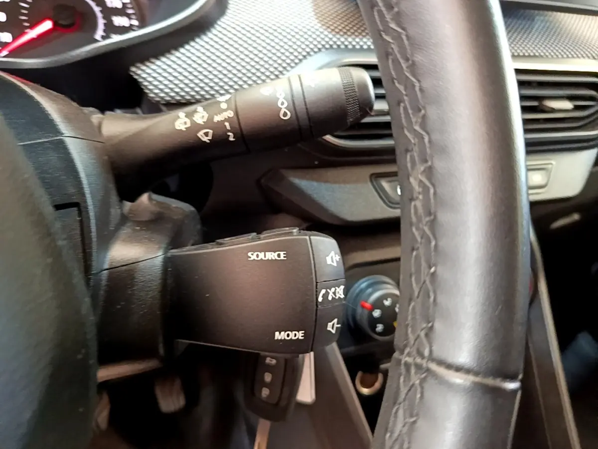 Gros plan intérieur sur le volant noir et la commande multimédia à gauche du tableau de bord de la Dacia Sandero blanche.